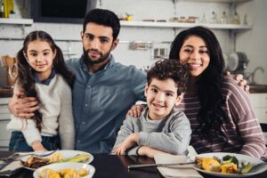 cheerful latino family smiling while looking at camera during lunch